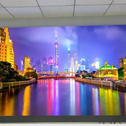 Titan all-in-one LED TV wall-mounted in a meeting room, displaying a vivid night cityscape