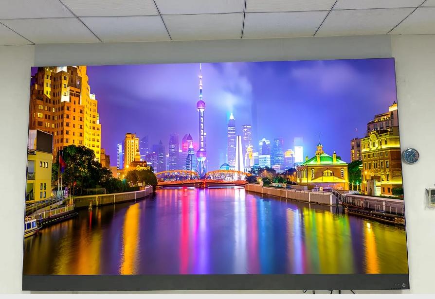 Titan all-in-one LED TV wall-mounted in a meeting room, displaying a vivid night cityscape